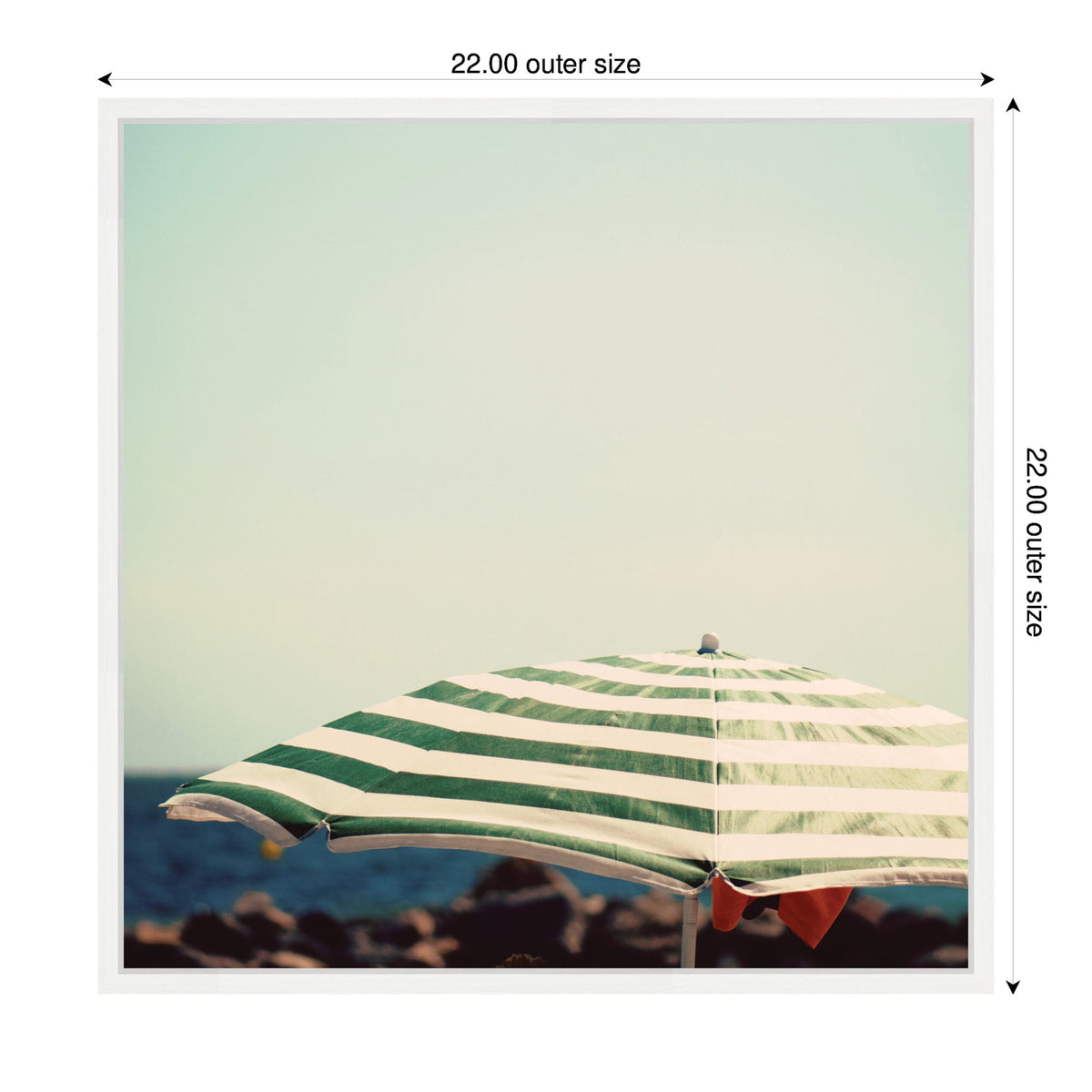 Green and white striped beach umbrella with a distant rocky shore and calm sky in the background, centered in a square frame with measured edges.
