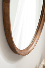 Close-up of the beveled edge of a round wall mirror with a smooth, medium brown wooden frame against a light wall surface.
