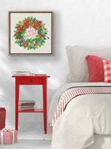 Square framed canvas featuring a colorful Christmas wreath with a red bow and "Happy Holidays" text, hanging above a red bedside table next to a beige bed with red and plaid pillows.