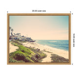 Framed vintage-style coastal beach scene showing sandy shore with green shrubbery and seaside houses under a clear sky, viewed from a low hillside.