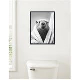 Black and white framed canvas of a capybara wrapped in a towel resembling a bathrobe, displayed above a white toilet in a bright bathroom.