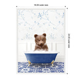 Young brown bear cub sitting in a blue clawfoot bathtub filled with bubbles, set against white wainscoting and floral wallpaper with blue leaves above patterned blue and white tile floor.