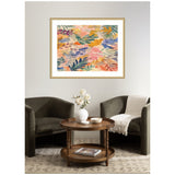 Abstract floral painting with layered leaf shapes in pink, orange, green, and blue hues displayed in a gold frame above two dark gray armchairs and a round wood table.