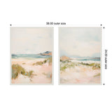 Two framed canvas paintings side by side depicting soft pastel beach landscapes with sandy dunes, green grasses, and a hazy sky over distant water.