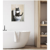 Framed artwork of a black cat sitting on a toilet holding a roll of toilet paper, displayed on a white wall above a modern white bathtub with a towel.
