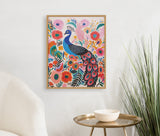 Framed print of a bright blue peacock surrounded by colorful pink, orange, and red flowers and green leaves on a white wall above a brass side table and white chair.