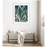 Abstract blue floral artwork with large cream and green leaf shapes framed in light wood, hanging above a wooden bench with a white folded blanket and open book.