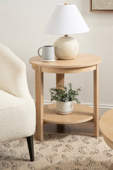 Round light wood side table with a spherical wood lamp topped by a white lampshade and a gray mug on top, plus a potted green plant on a lower shelf