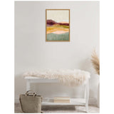 Abstract framed canvas with horizontal layers in burgundy, orange, yellow, and green hues, hanging above a white bench draped with a fluffy off-white throw.