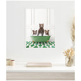 Three brown bear cubs sitting in a vintage green clawfoot bathtub against white paneled walls and green patterned tile floor, framed and displayed above a white shelf.