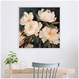 Square framed painting of soft peach-pink peonies with dark green leaves against a deep green background, hung above a light wood desk with a plant and wire decor.
