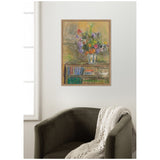 Framed pastel painting of colorful flowers in a glass vase sitting on a table with books beneath, hung on a white wall above a dark green armchair with a knitted throw.