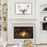Modern white mantel fireplace with a bright fire, framed canvas showing a stag's antlered head above, flanked by white built-in shelves with decorative items.