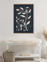 Framed canvas artwork of two stylized birds perched on white and green leafy branches with brown circular patterns on a dark background, hanging above a white bench with a soft white fur throw.
