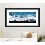 Framed aerial photograph of turquoise ocean waves crashing onto a black sand beach, with white sea foam creating dynamic patterns at the shoreline.