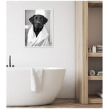 Black and white framed photograph of a black labrador wrapped in a white towel, hanging above a modern white bathtub with a towel draped over the side.