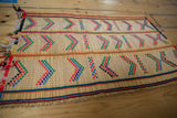 Flat woven vintage Tuareg rug mat with geometric arrow patterns in red, blue, green, and black on beige, displayed on wooden floorboards.