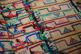 Close-up of a woven rug with a grid pattern containing small triangle designs in red, blue, and green, accented by colorful tassels and black outlines.