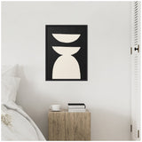 Abstract geometric art with two beige, curved shapes stacked vertically on a black background, framed in black, hanging on a white wall above a wooden bedside table.