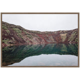 Calm water reflecting rugged, multicolored rocky cliffs under overcast sky in a natural pool setting, framed in simple brown wood.