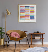 Framed canvas with colorful horizontal wavy lines arranged in columns, hanging above a tan leather chair with a round pink pillow, next to a wooden side table and brass floor lamp.