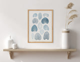 Wall art featuring abstract blue coral and shell shapes in various shades, framed in light wood above a simple wooden shelf with white ceramic vases and dried grasses