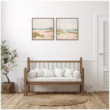 Two square framed canvas prints above a wooden bench with white cushions in a minimalist room with natural wood floors and neutral decor.