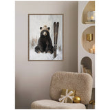 Framed canvas of a black bear wearing a knitted hat sitting next to upright skis, mounted on a neutral wall above a cozy beige textured chair with gold-accented decor nearby.