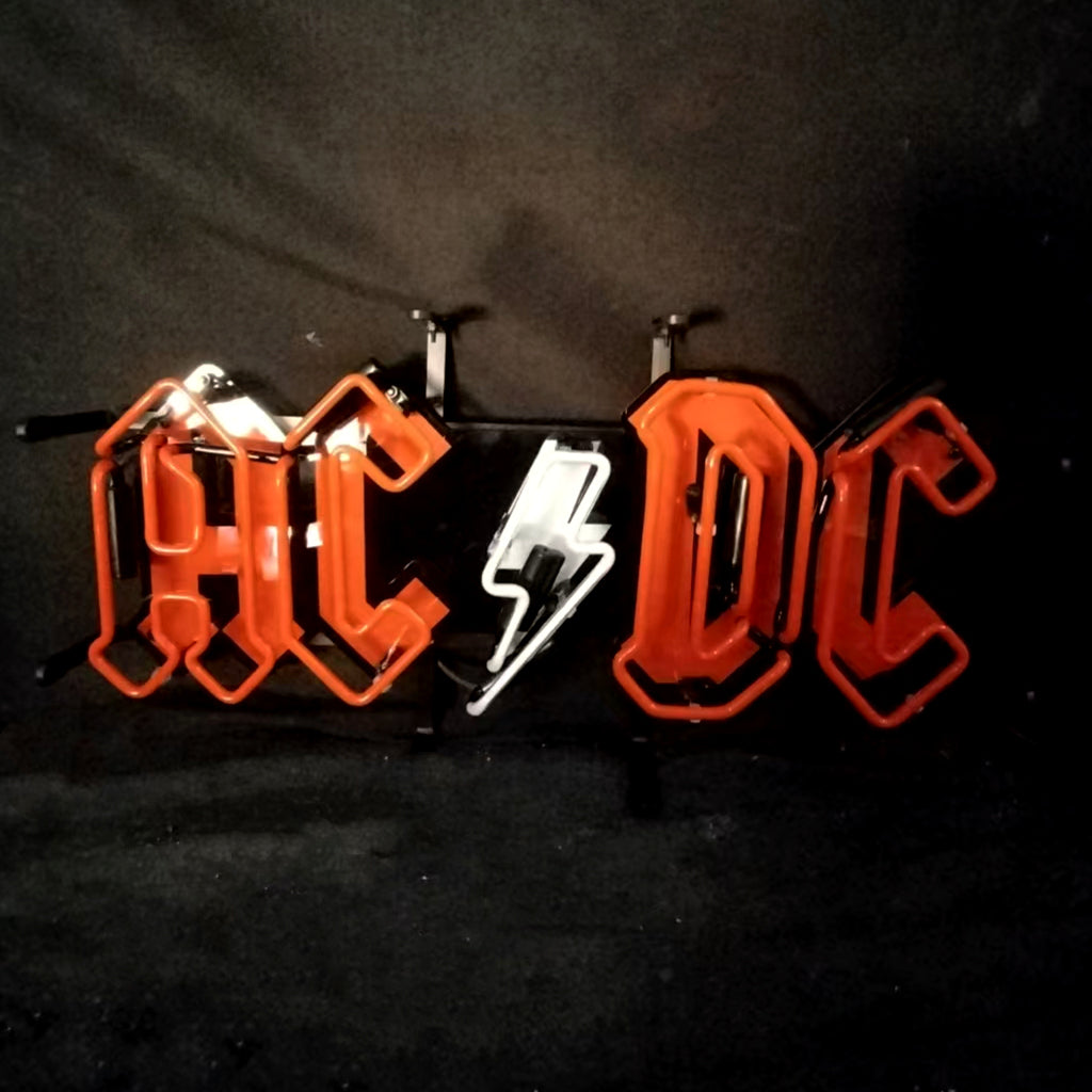 Neon sign spelling 'AC DC' in bright red Gothic script with a white lightning bolt symbol in the center against a black background.