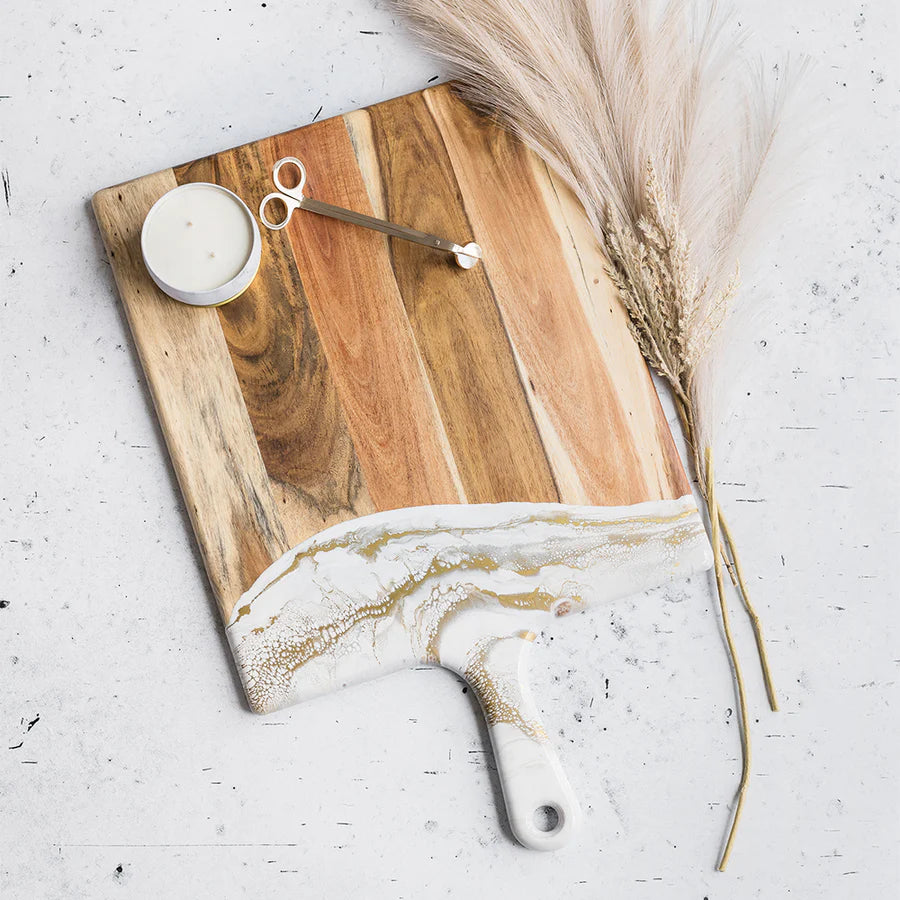 Wooden charcuterie serving tray with marbleized edge on a light gray surface with a candle and dried pampas grass.