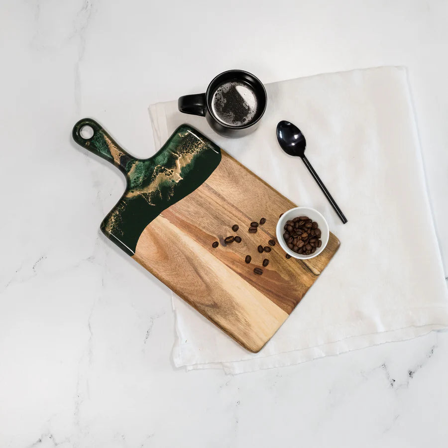 Wooden resin charcuterie board with green handle, coffee beans, and a small bowl on a white marble surface.