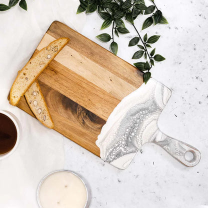 Wooden resin charcuterie board with bread slices, a cup of coffee, and a jar on a light surface with greenery.