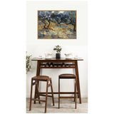 Framed print of Van Gogh's Olive Trees with swirling blue and green textured brushstrokes above a dark wood bar table holding white mugs and a small potted plant, paired with two matching stools.