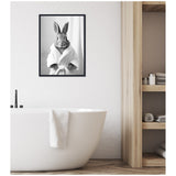 Minimalist bathroom with white freestanding tub, black faucet, white towel hanging over tub, and framed black-and-white photo of a rabbit in a bathrobe on textured white wall