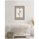 Framed abstract canvas print with two beige organic shapes on gray background, hanging above a white bench draped with cream fur, a taupe bag below, and pampas grass to the side.