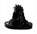 Black Adiyogi statue with flowing hair details, mounted on an oval base with a small gold-colored adornment near the top left.