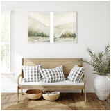 Two-piece framed canvas wall art depicting soft, muted winter landscapes with foggy mountains and pine trees, hung side-by-side above a wooden bench with black-and-white checkered pillows.
