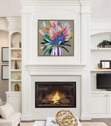 Framed bright floral painting with pink, blue, and yellow brushstrokes in a striped purple and white vase hanging above a lit fireplace in a white built-in cabinetry room.