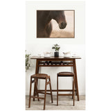 Framed canvas print of a dark horse's nose and neck with warm, soft background above a wooden table set with white bowls, glasses, a small plant, and two wooden stools.