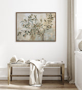 Abstract canvas painting of an olive tree branch with muted green and beige leaves in a wooden frame, hanging above a woven bench with a draped white blanket.