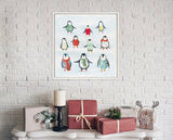 Framed canvas with nine colorful penguins wearing winter scarves and sweaters, hung on a white brick wall above wrapped holiday gifts and a candle on a white table.