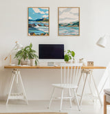 Home office setup with a wooden desk supported by white sawhorse legs, a white chair, twin landscape paintings with blue and green hues, and potted plants on the desk.