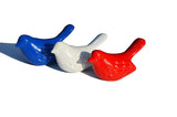 Three ceramic bird figurines in blue, white, and red colors, arranged side by side casting shadows on a white surface.