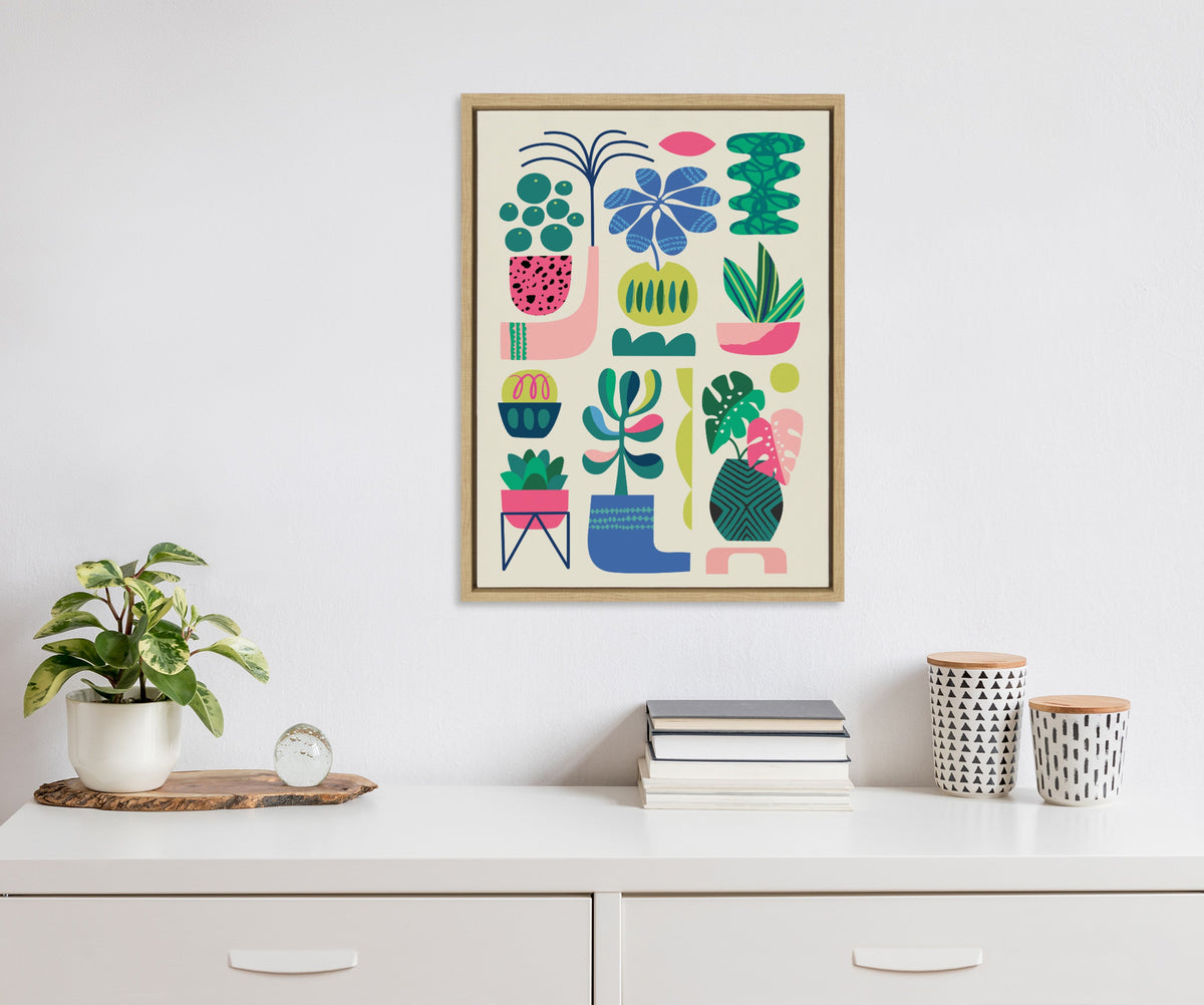 Colorful abstract plant shapes in pots and vases on a cream background, framed and hung above a white dresser with potted plant and patterned jars.
