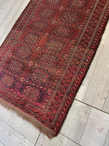 Antique 1880s Baluch rug with deep red and brown geometric patterns framed by multiple patterned borders, displayed on light wood flooring.