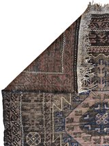 Corner view of an antique 1880s Baluch tribal wool rug with geometric patterns in brown, blue, and beige, featuring fringed edges and a folded-over corner.