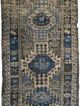 Rectangular Baluch tribal rug with central medallions in muted blue, beige, and brown, featuring geometric motifs and patterned borders.