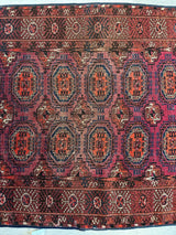 Antique 1910s Tribal Turkoman rug with repeating red and orange geometric medallions on a purple background, framed by detailed red and brown patterned borders.