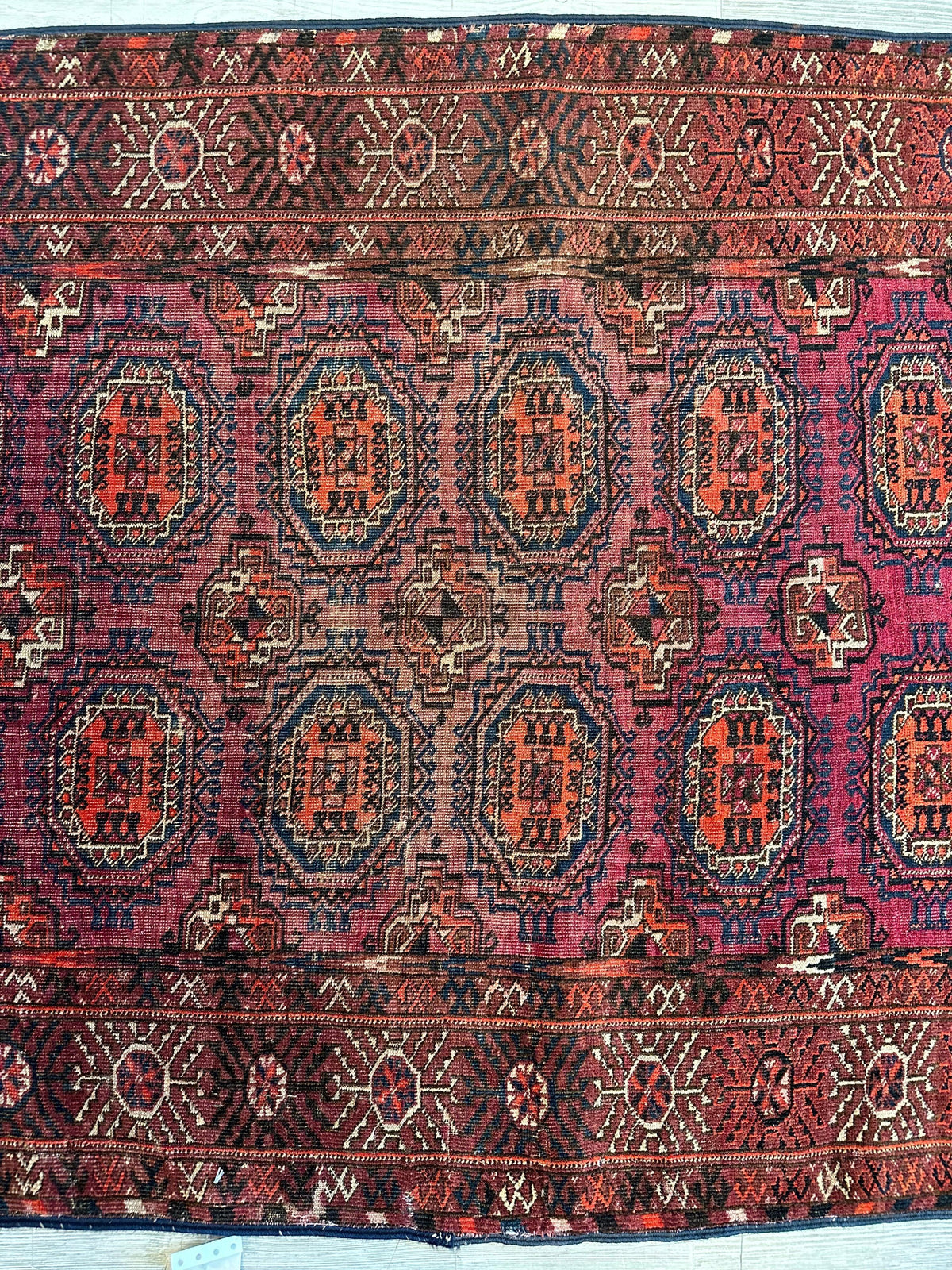 Antique 1910s Tribal Turkoman rug with repeating red and orange geometric medallions on a purple background, framed by detailed red and brown patterned borders.