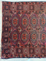 Antique 1910s Tribal Turkoman rug with geometric medallions in red, orange, and navy blue, bordered by intricate floral and star motifs on a dark red field.